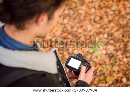 Photographer looking through pictures on his camera standing in an autumn forest