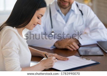 Close up smiling female patient signing medical form at meeting in clinic with male doctor, sitting at desk, satisfied woman putting signature on health insurance agreement, healthcare concept