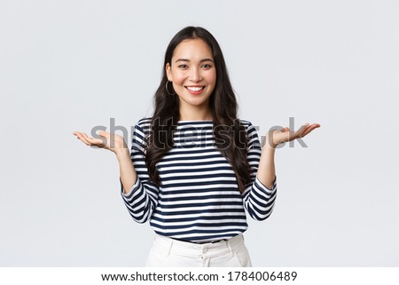 Lifestyle, people emotions and casual concept. Cute smiling asian woman introduce two products, hold hands sideways as if demonstrating products on palms, standing white background