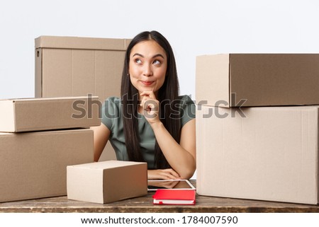 Small business owners, startup and e-commerce concept. Thoughtful creative asian woman open internet store, thinking how make profit, better income, sitting near lots of boxes ready for shipping