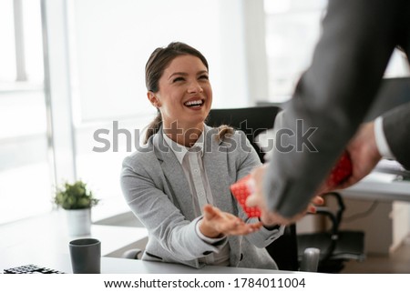 Young businessman giving his colleague present in office. Young man surprise beautiful businesswoman in office.