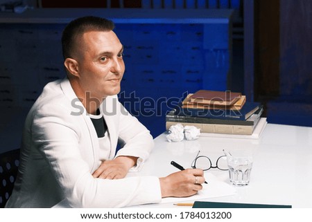 Businessman 30-35 years old in a white jacket signs important documents while sitting at the table. Closeup male portrait. Business and deal concept.