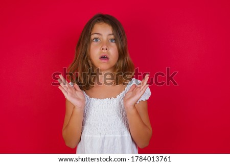 Surprised terrified little female isolated over red background. Gestures with uncertainty, stares at camera, puzzled as doesn't know answer on tricky question, People, body language