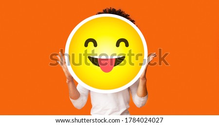 Black bushy man holding happy cheeky emoji emoticon smiley in front of his head, standing over orange studio background, creative collage, empty space Royalty-Free Stock Photo #1784024027