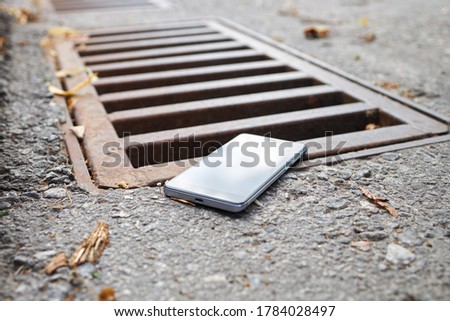lost smart phone device laying on the ground near rain drain at city street.  Royalty-Free Stock Photo #1784028497