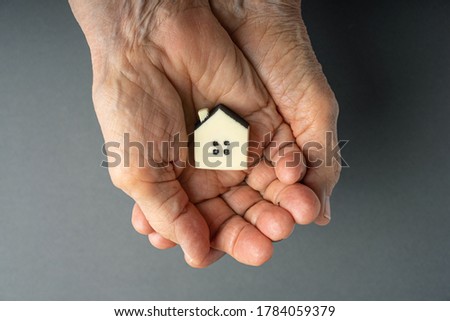 Inheritance concept. Elderly woman hands holds a little toy house. Inherited property idea. Royalty-Free Stock Photo #1784059379
