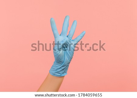 Profile side view closeup of human hand in blue surgical gloves showing number four 4 with hand. indoor, studio shot, isolated on pink background.