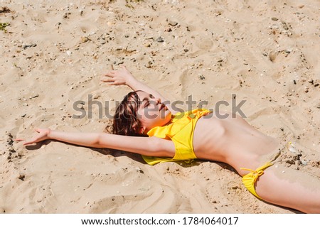 Young woman lies in summer on the beach. The girl lies on the sand on the beach. Teenager at sea. Vacation, summer, vacation, vacation. Child in a yellow swimsuit. Happinnes exists, Enjoying life