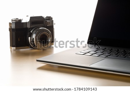 Retro analog SLR camera next to laptop on wooden desk in office, digital photography or image processing concept, selective focus