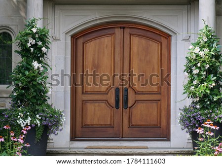 Elegant wooden double front door with curved top, surrounded by flowers Royalty-Free Stock Photo #1784111603