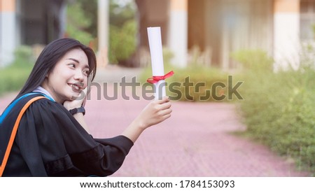 Portrait of happy and excited of young Asian female university graduate wears graduation gown and hat celebrates with degree in university campus in the commencement day. Education stock photo.