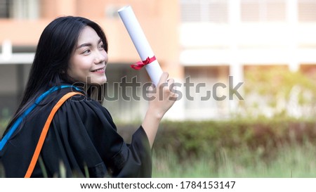 Portrait of happy and excited of young Asian female university graduate wears graduation gown and hat celebrates with degree in university campus in the commencement day. Education stock photo.
