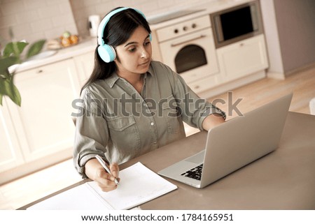 Indian woman student wear headphones learning online watching online class webinar seminar training looking at laptop computer elearning remote lesson writing notes, video conference calling at home. Royalty-Free Stock Photo #1784165951