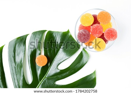 Colored balls of fruit marmalade on a green fresh leaf of tropical monstera on a white background. the view from the top. a copy of the space.