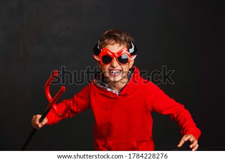 Happy Halloween.. child dressed in a devil costume with a red pitchfork in his hands in the image of the devil scares at a Halloween party. Preparing for Halloween. Trick or treat