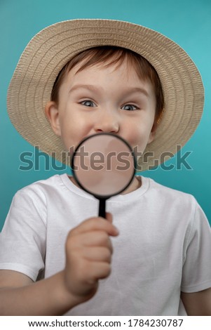 Close-up portrait of a cute boy looking through a magnifying glass-isolated on a blue background.