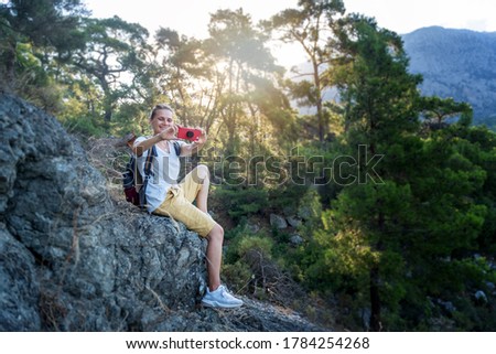 Young woman traveler makes photos on a smartphone while walking in the forest and enjoying nature and solitude, travel and summer adventures.