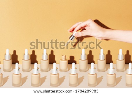 A female hand holds a dropper for applying bb foundation cream. Opened and closed jars of a cosmetic makeup product on a beige background. Pattern of beauty products packaging Royalty-Free Stock Photo #1784289983