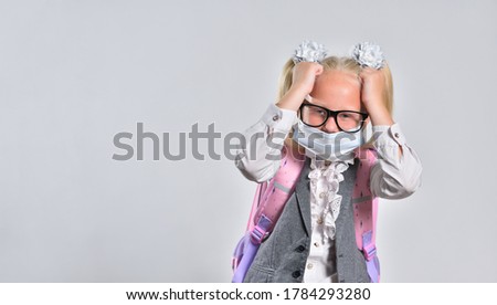 Funny schoolgirl in a protective mask is tired and holding her head.