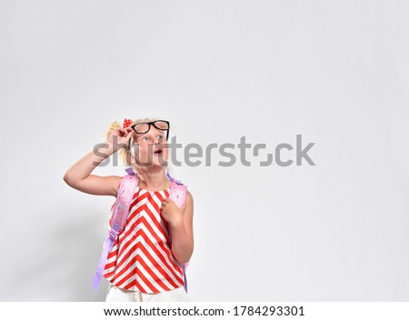 Schoolgirl 7 years old looks up in surprise raising her glasses on a gray background, studio photography.