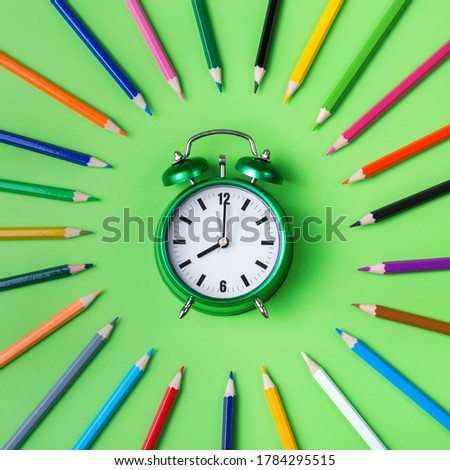 Assortment of colourful rainbow pencils and alarm clock on a mint green background. Top view flat lay. Back to school concept