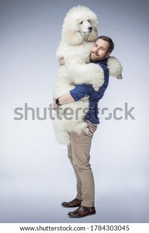 happy white guy holds a white poodle puppy in his arms. A man smiles at his dog in the isolated background. The dog and its owner. Royalty-Free Stock Photo #1784303045