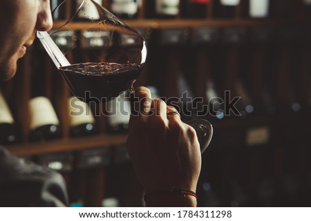 Close-up shot of young sommelier smell red wine on wine cellar background. Royalty-Free Stock Photo #1784311298