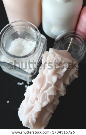 Home made powder pink candle, roses shape. Bath salt and cosmetics around. Black background. 
