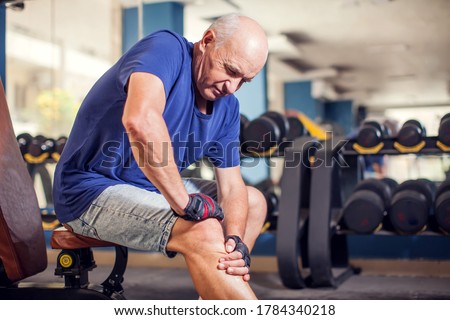 A portrait of bald senior man feeling strong knee pain during training in the gym. People, healthcare and lifestyle concept Royalty-Free Stock Photo #1784340218