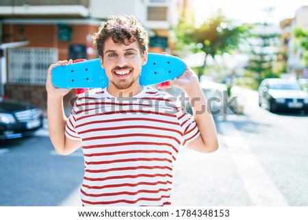 Young caucasian skater man smiling happy holding skate walking at street of city.