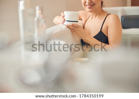 Cropped photo of a woman taking a bath with a beauty product in her hands