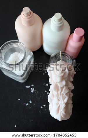Home made powder pink candle, roses shape. Bath salt and bottles of perfume around. Black background. 