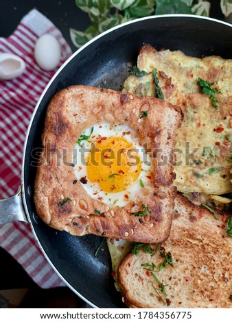 Egg in a hole and Egg sandwiches on a pan with herbs and chilli flakes.