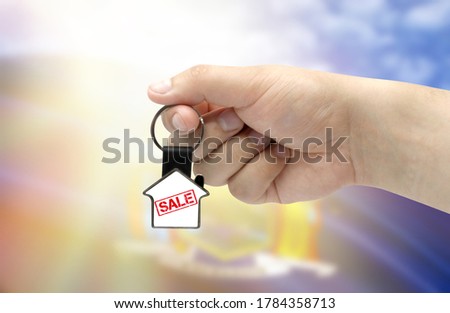 A man's hand holds a keychain in the form of a house with the inscription Sale on the background of the flag of State of New York. Property and real estate sale concept.