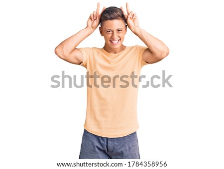 Young handsome man wearing casual clothes posing funny and crazy with fingers on head as bunny ears, smiling cheerful 