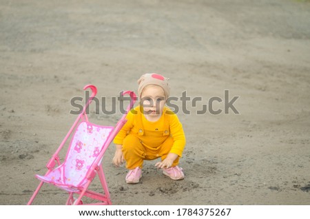 Photo of a toddler girl in a funny hat playing with a toy stroller
