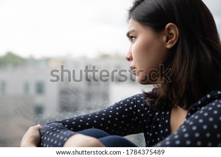 Sad Asian millennial girl look in window distance thinking or pondering alone at home, thoughtful upset unhappy Vietnamese woman lost in thoughts dreaming, feel lonely distressed, loneliness concept Royalty-Free Stock Photo #1784375489
