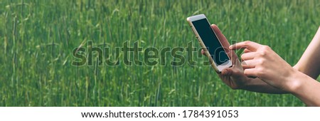 Banner, Smartphone in the hands of a girl, against the background of a green field.
