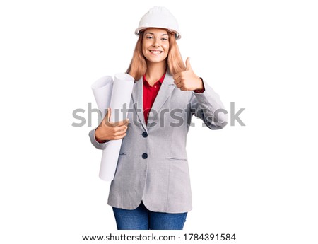 Beautiful young woman wearing architect hardhat holding build project smiling happy and positive, thumb up doing excellent and approval sign 