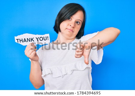 Brunette woman with down syndrome holding thank you paper with angry face, negative sign showing dislike with thumbs down, rejection concept 