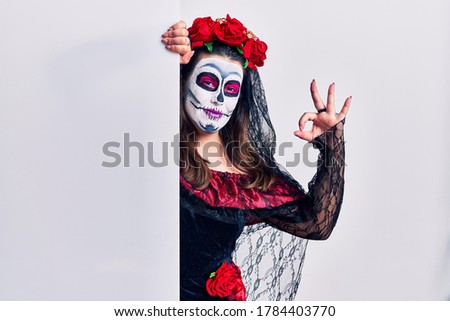 Young woman wearing day of the dead custome holding blank empty banner smiling positive doing ok sign with hand and fingers. successful expression. 