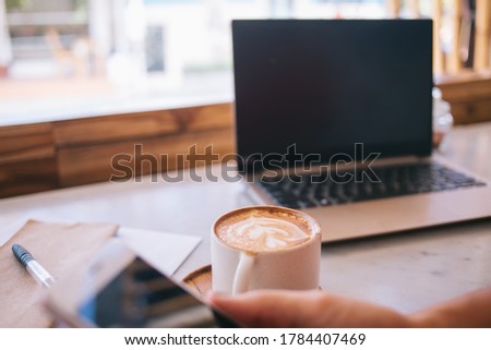 Cropped female blogger using wireless 4g connection on smartphone and laptop technology, freelance woman reading web article during mobile social networking sitting at cafeteria table with cappuccino