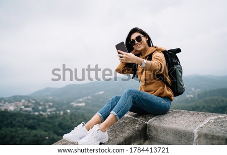 Cheerful asian girl in sunglasses resting during vacation trip visiting historical place making picture on smartphone, happy female tourist posing for selfie using mobile phone camera on destination
