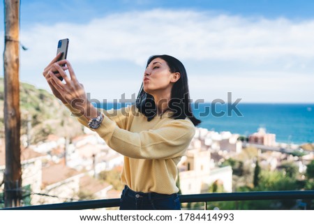 Attractive Asian hipster tourist making duck face grimace during travel vacations, beautiful teenage vlogger shooting video showing kiss to front camera during sightseeing to overlooking area