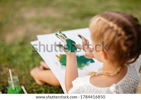 Cute little caucasian kid girl drawing or painting with colored paints in park. Kindergarten children education, back to school after coronavirus pandemic. Social distancing during covid-19 epidemic