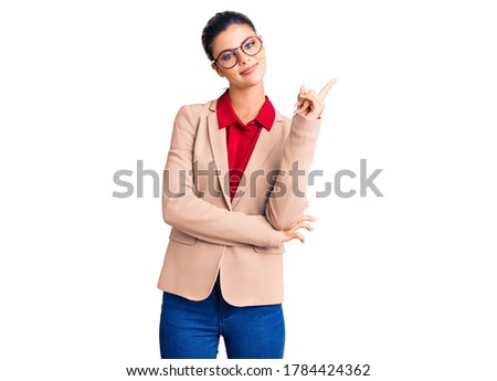 Young beautiful woman wearing business shirt and glasses with a big smile on face, pointing with hand and finger to the side looking at the camera. 