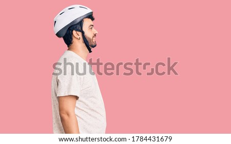 Young hispanic man wearing bike helmet looking to side, relax profile pose with natural face with confident smile. 