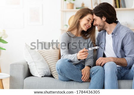Happy family concept. Married couple bonding on couch and holding positive pregnancy test, home interior, free space Royalty-Free Stock Photo #1784436305