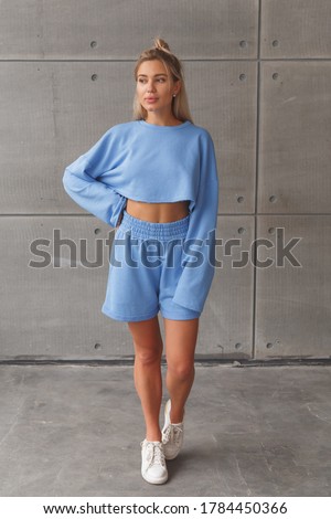 Young caucasian blonde in a fashionable sportswear look on woman. Blue shorts and sweatshirt.