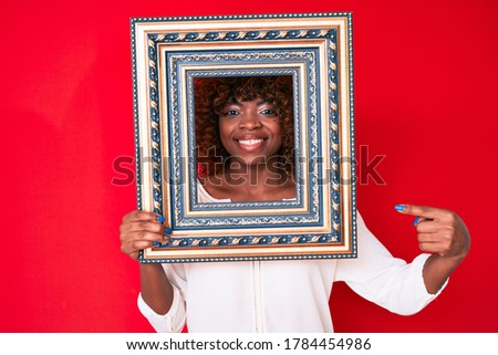 Young african american woman holding empty frame smiling happy pointing with hand and finger 
